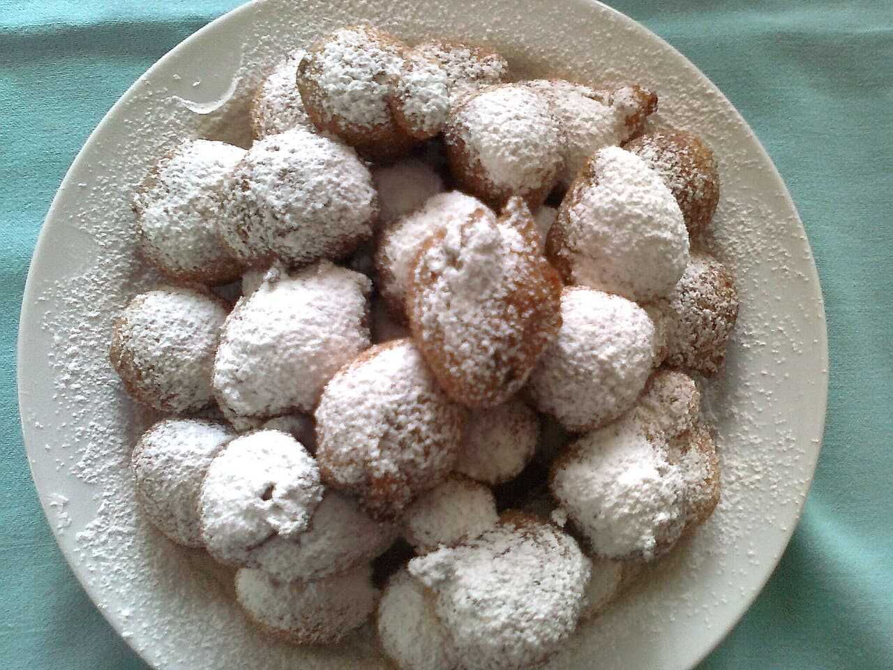 A pile of golden fritule dusted with icing sugar on a plate