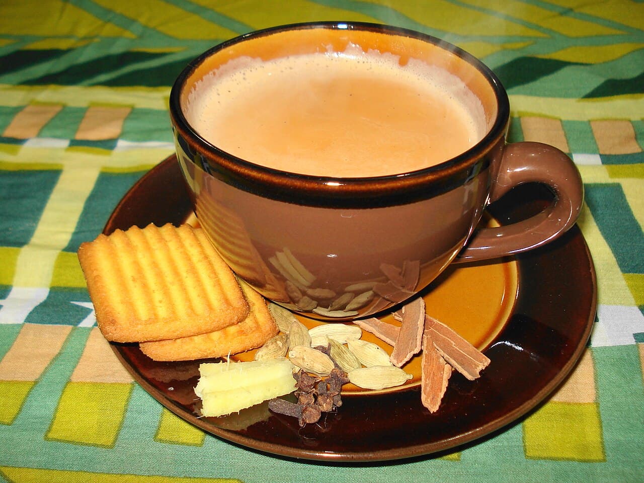 Two small glass cups of rich golden karak chai on a wooden tray with cardamom pods