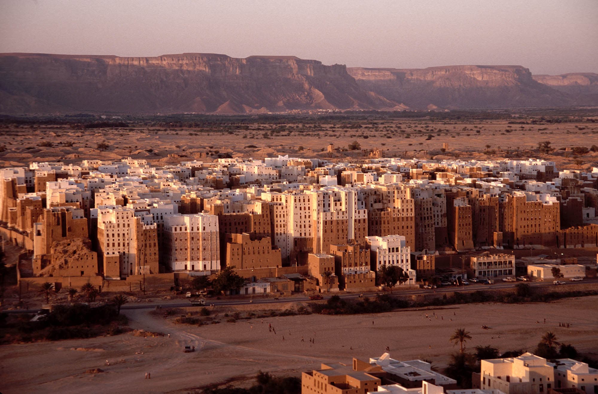 A wadi village of mud-brick houses nestled at the base of towering sandstone cliffs in Hadhramaut