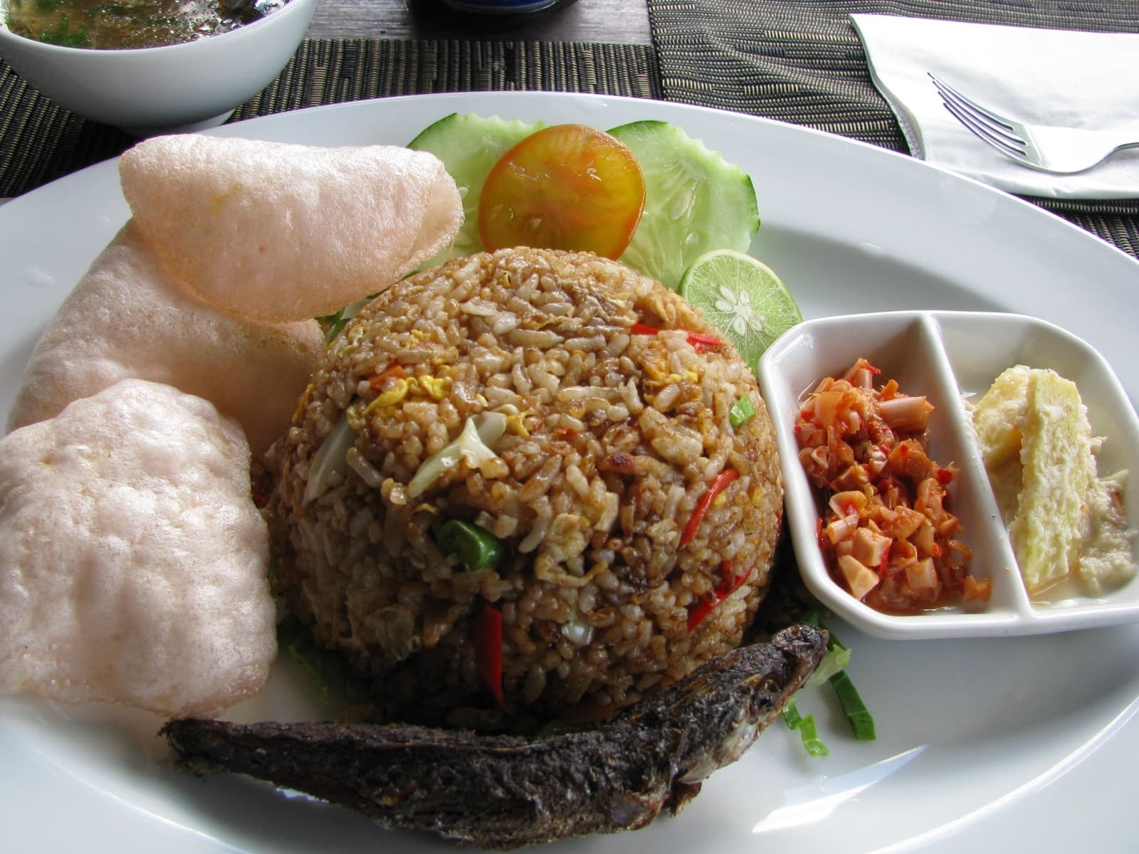 A plate of golden-brown nasi goreng with prawn crackers, cucumber and tomato