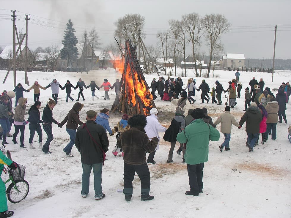People in colourful folk costumes and frightening masks celebrating Užgavėnės in a snowy village square