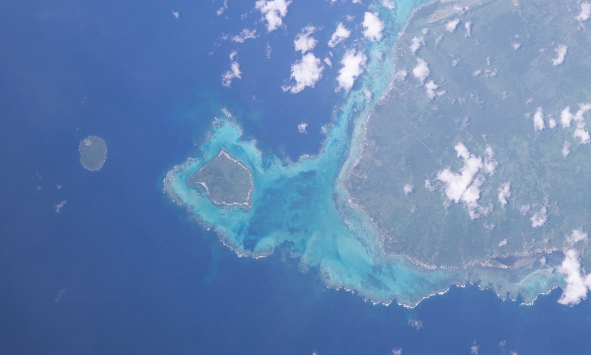 A small green island viewed from the water with clear blue sea in the foreground